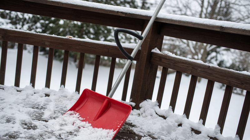 A red snow shovel with a second curved handle leaning on a snowy deck railing, in Truckee, California
